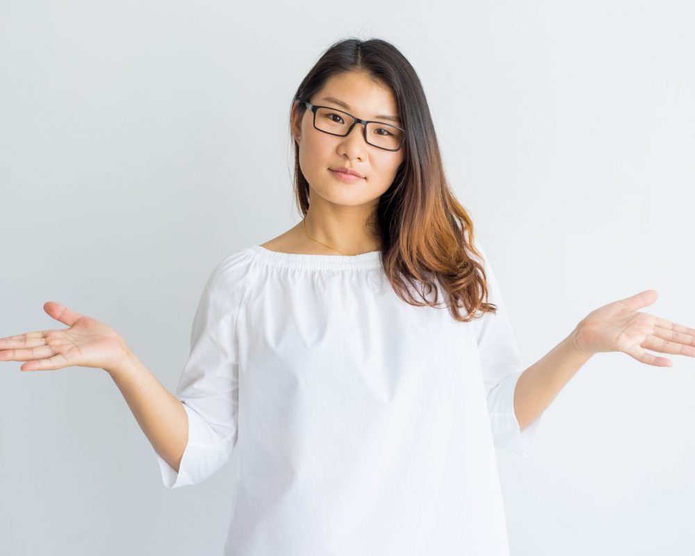 Puzzled Chinese student girl shrugging shoulders and looking at camera. Misunderstanding beautiful Chinese woman in loose shirt gesturing. Incomprehension concept