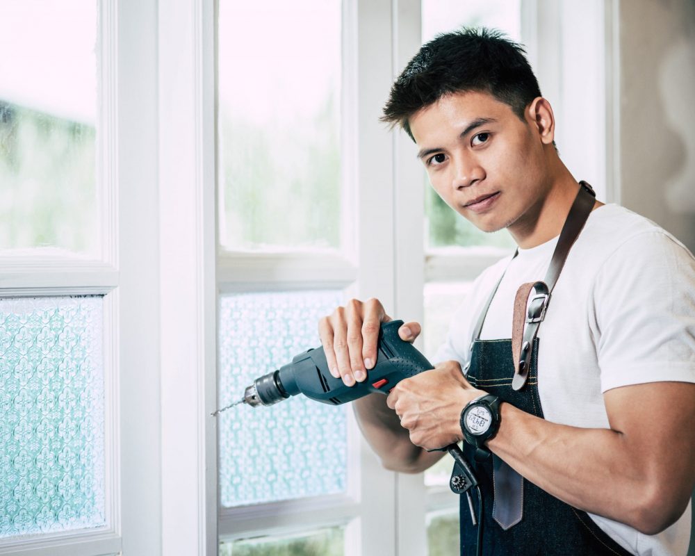 The carpenter holds the drill and drills the window. The carpenter holds the drill and drills the window. Selective focus.